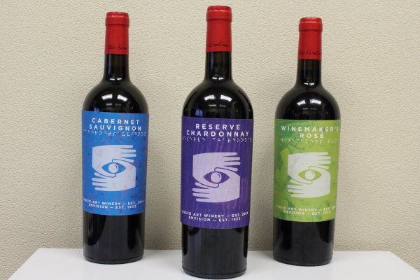 Three wine bottles on a table wrapped in Envision Arts labels.