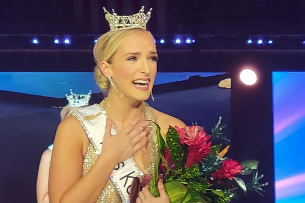 Courtney wearing her Miss Kansas crown and sash, holding her flowers and smiling and crying after her named was called as the winner.