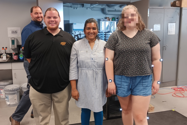 Sarika standing with a research participant who has motion sensors taped on her body.