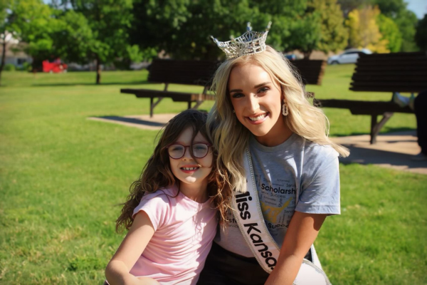 Courtney smiling as she wears her crown hugging a young child with glasses.