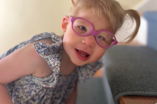 Charlotte wearing pink glasses with her hair styled in two pigtails, her face close up to the camera and she laughs while looking at the camera.