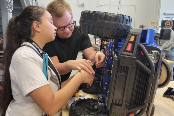 A young girl who is blind being shown how to work on a GoBabyGo car.