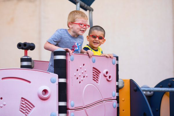 Two visually impaired children laughing playing on a playground.