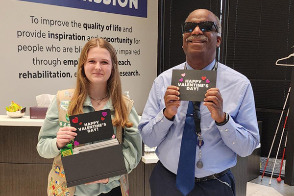 Clara Coppinger standing by Envision Dallas employee, Sam, show off their accessible valentines.