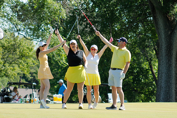 Golf team dressed in yellow celebrate a good shot on the green.